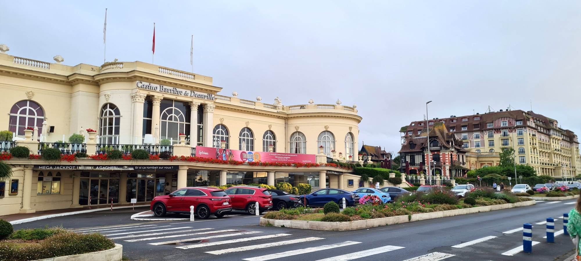 The cream façade of the Casino Barrière Deauville with arched windows, flags and a terrace, beside a street in Deauville