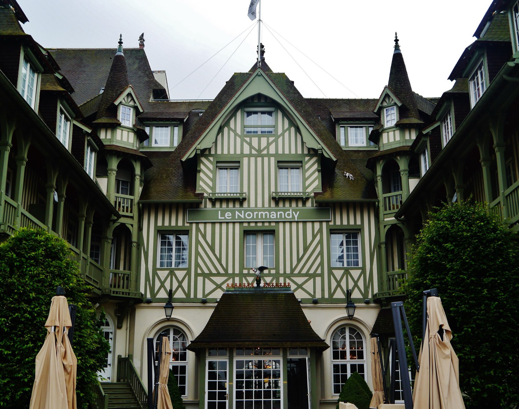 The half-timbered Anglo-Norman façade of Hôtel Barrière Le Normandy in Deauville, with its central gable, turrets and courtyard parasols